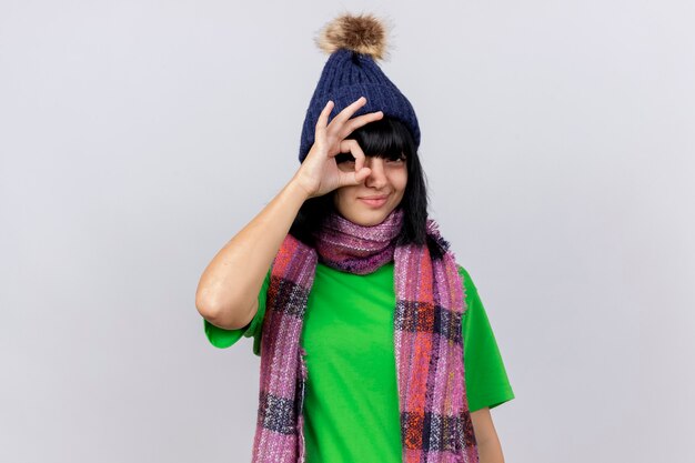Confident young ill caucasian girl wearing winter hat and scarf  doing look gesture isolated on white wall with copy space