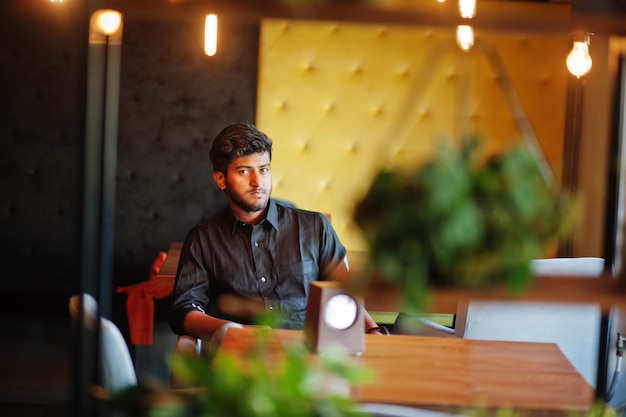 Free photo confident young indian man in black shirt sitting at cafe