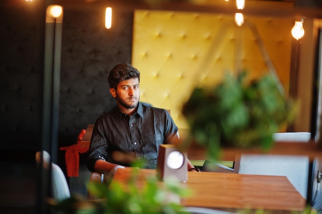 Confident young indian man in black shirt sitting at cafe