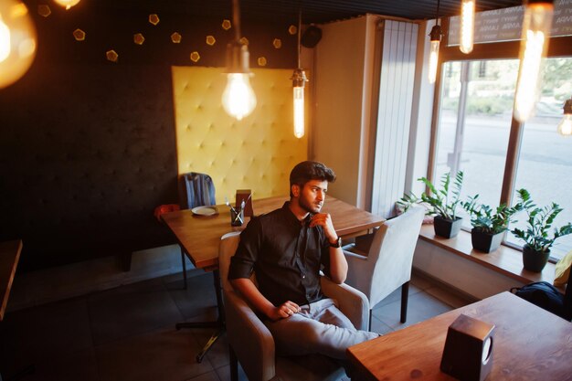 카페에 앉아 검은 셔츠에 자신감이 젊은 인도 남자