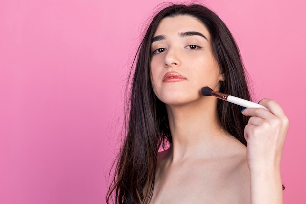 Confident young lady doing makeup on pink background High quality photo