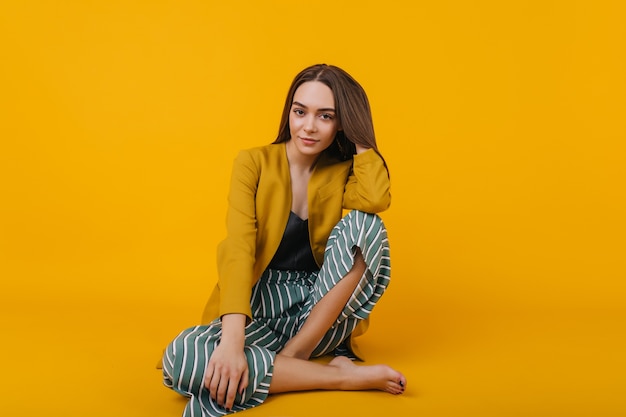 Confident young lady in striped pants sitting. glad white girl wears yellow jacket.