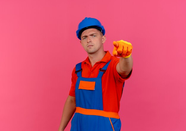 Confident young male builder wearing uniform and safety helmet in gloves showing you gesture 