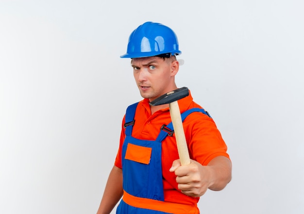 Confident young male builder wearing uniform and safety helmet holding out hammer