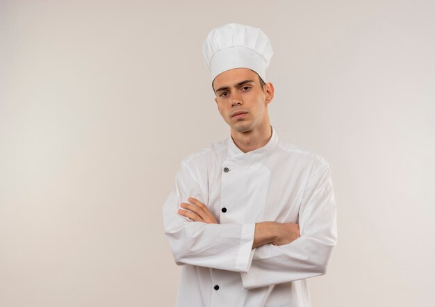 복사 공간이 격리 된 흰 벽에 요리사 유니폼 횡단 손을 입고 자신감 젊은 남성 요리사