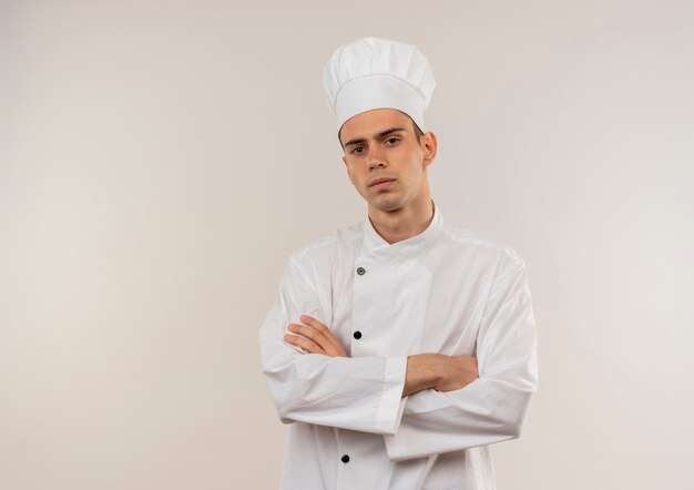 Confident young male cook wearing chef uniform crossing hands on isolated white wall with copy space