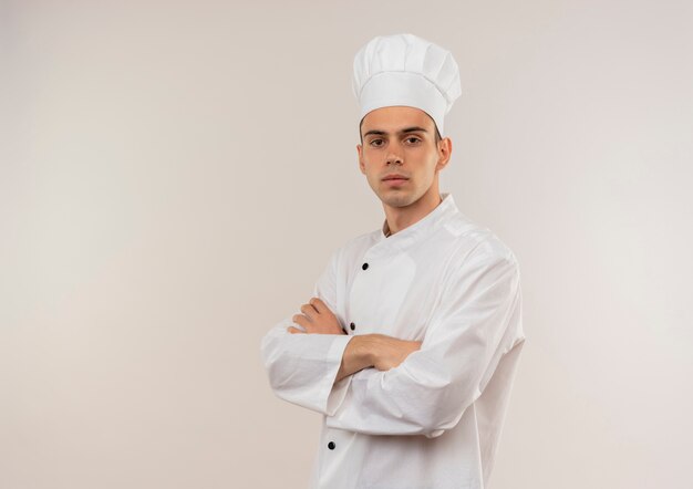 コピースペースと孤立した白い壁にシェフの制服の交差する手を着て自信を持って若い男性料理人