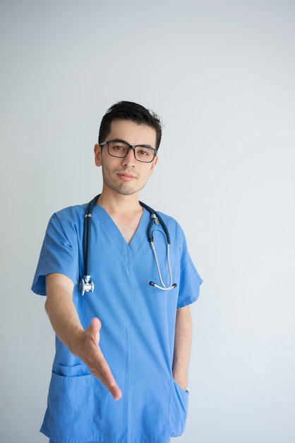 Confident young male doctor extending arm for handshake. Friendly doctor concept.