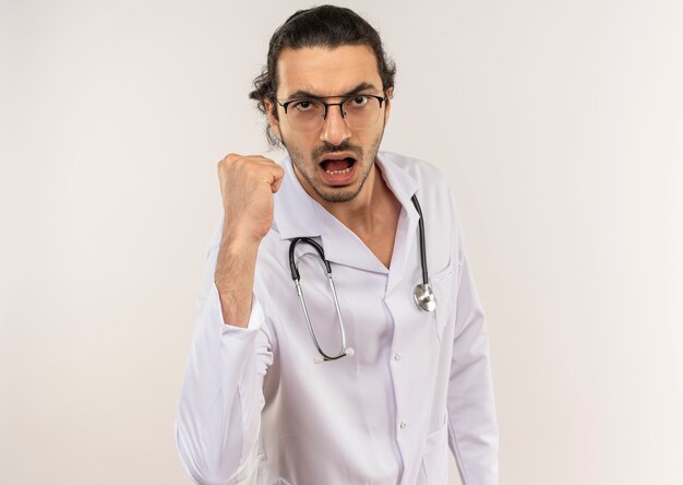 Confident young male doctor with optical glasses wearing white robe with stethoscope showing yes gesture