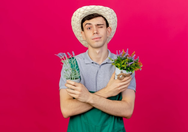 Бесплатное фото Уверенный молодой мужчина-садовник в садовой шляпе моргает и скрещивает руки