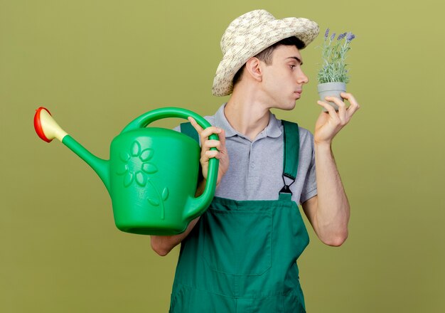 Free photo confident young male gardener wearing gardening hat holding and sniffing flowers