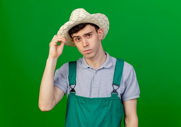 コピースペースと緑の背景に分離されたガーデニング帽子を身に着けて保持している自信を持って若い男性の庭師