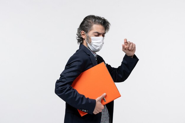 Confident young male in suit and holding his documents wearing his medical mask closing his eyes on white surface