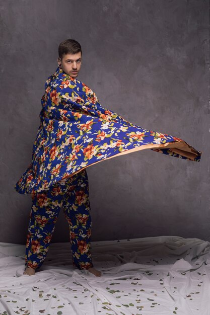 Confident young man blowing his floral drape against grey wall