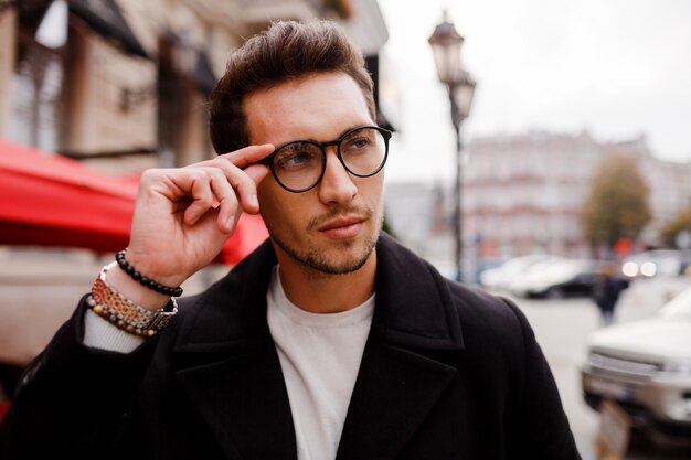 Confident young man in full suit looking away while standing outdoors in european city. Wearing eyewear. Stylish hairstylr.