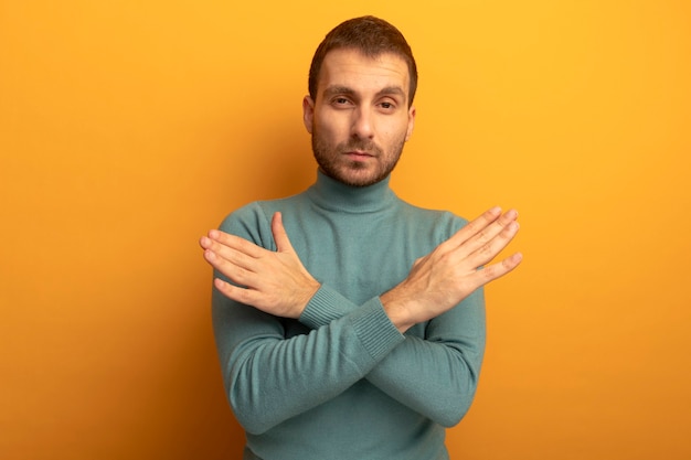 Confident young man looking at front keeping hands crossed in air isolated on orange wall