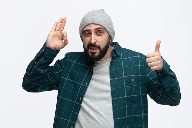 Free photo confident young man wearing winter hat looking at camera showing thumb up and ok sign isolated on white background