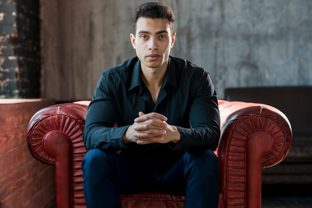 Confident young man with his hand clasped sitting on cozy armchair