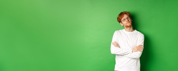 confident young man with red hair wearing glasses looking smug at right side copy space cross arms o