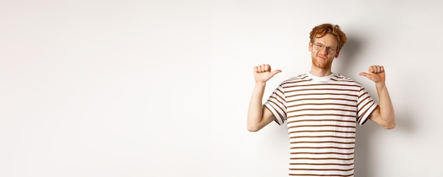 Free photo confident young nerdy guy in glasses with red hair pointing at himself and looking like professional