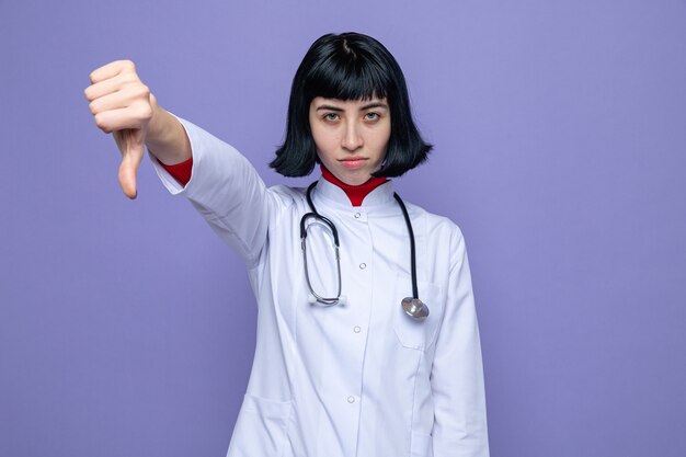 聴診器の親指を下に向けて医者の制服を着た自信を持って若いかなり白人の女の子