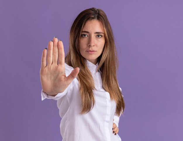 Уверенная молодая красивая кавказская девушка жестикулирует знак остановки на фиолетовой стене с копией пространства
