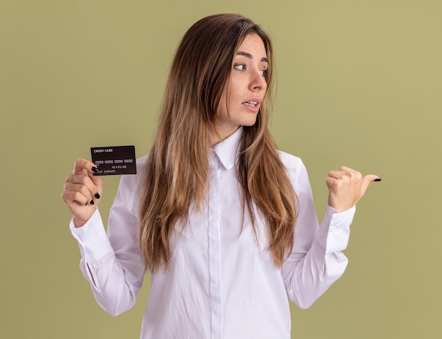 Free photo confident young pretty caucasian girl holds credit card looking and pointing at side