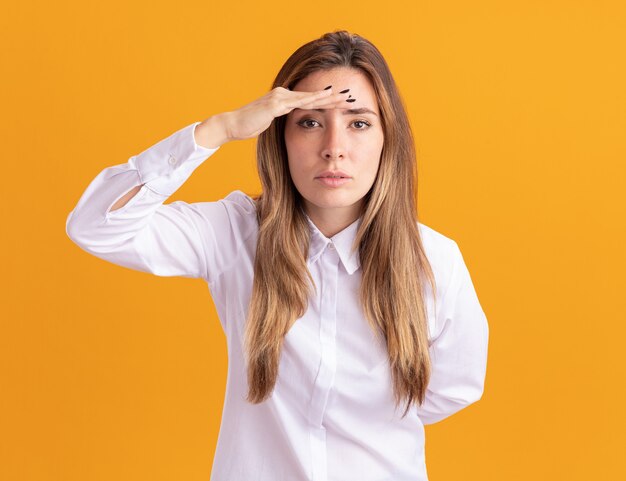 Confident young pretty caucasian girl keeps palm at forehead looking at camera on orange 