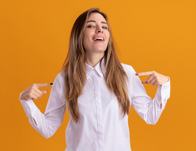 Confident young pretty caucasian girl points at herself with two hands isolated on orange wall with copy space