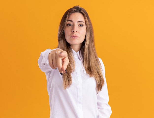 Confident young pretty caucasian girl points isolated on orange wall with copy space