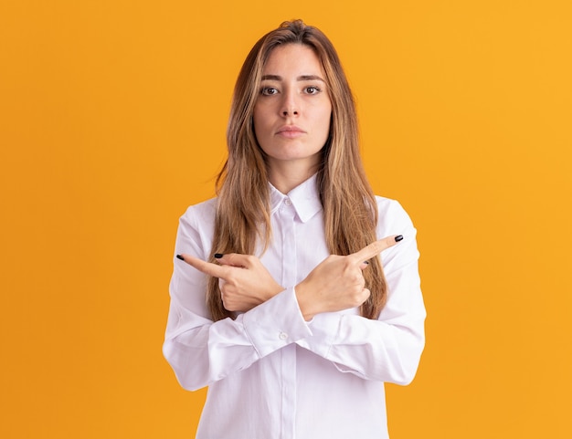 Confident young pretty caucasian girl points at sides isolated on orange wall with copy space