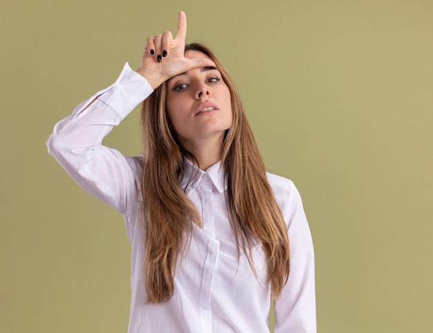 Confident young pretty caucasian girl puts hand on forehead gesturing loser sign