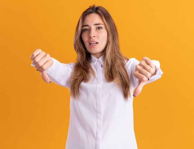 Confident young pretty caucasian girl thumbs down with two hands on orange 