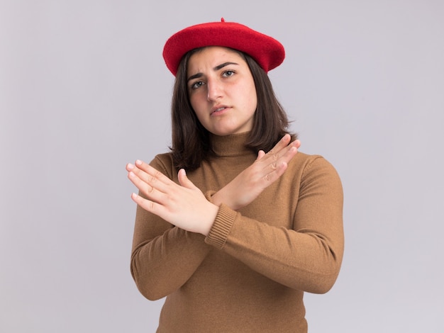 Confident young pretty caucasian girl with beret hat crossing hands gesturing no sign