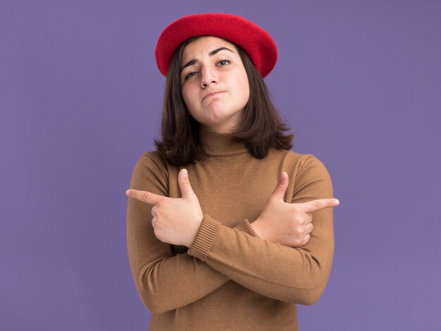 Confident young pretty caucasian girl with beret hat pointing at sides on purple