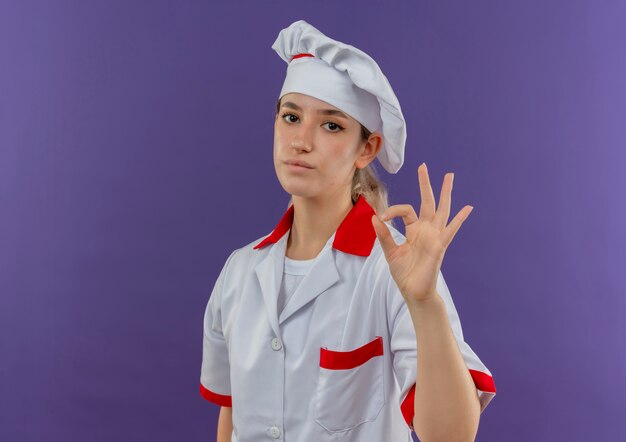Confident young pretty cook in chef uniform doing ok sign looking  isolated on purple wall with copy space