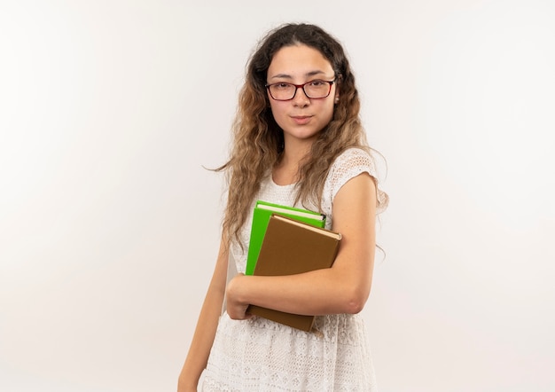 Уверенная молодая симпатичная школьница в очках и задней сумке, держащая книги, выглядящие изолированными на белом с копией пространства