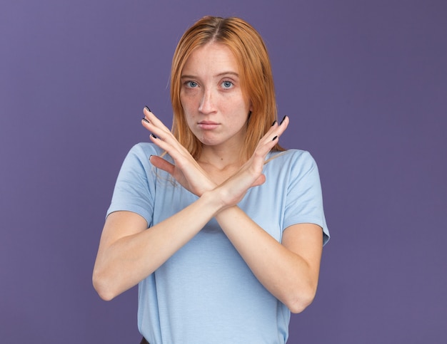 Free photo confident young redhead ginger girl with freckles crossing hands gesturing no sign on purple