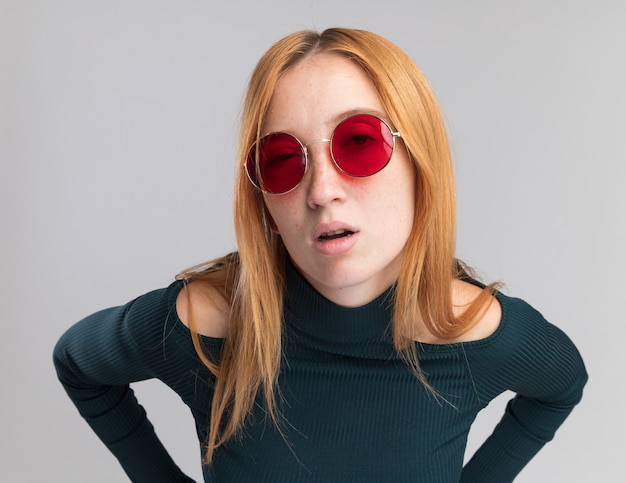 Confident young redhead ginger girl with freckles in sun glasses looking at camera on white