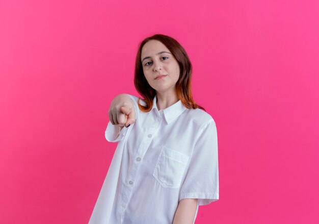 Confident young redhead girl showing you gesture isolated on pink background