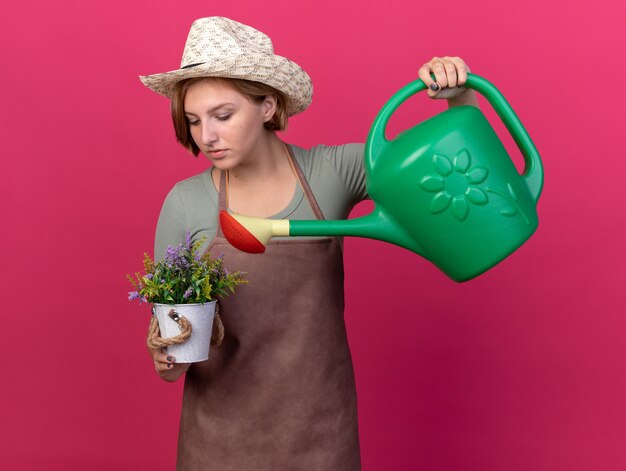 じょうろと植木鉢で花に水をまく園芸帽子を身に着けている自信を持って若いスラブの女性の庭師