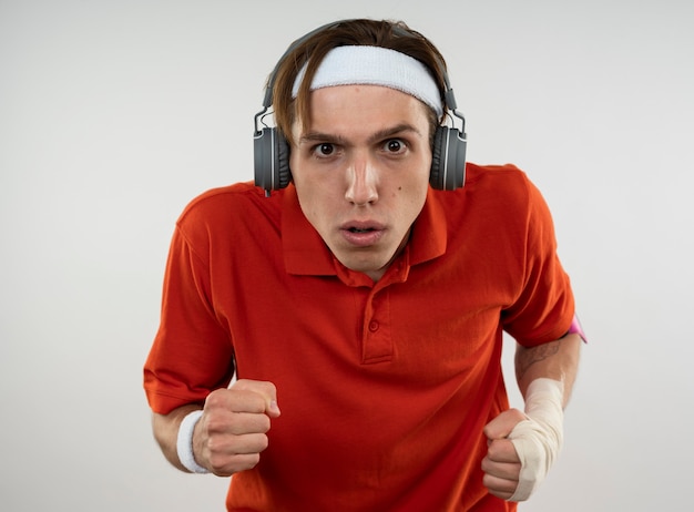 Free photo confident young sporty guy wearing headband with wristband and headphones with phone arm band showing running gesture isolated on white wall