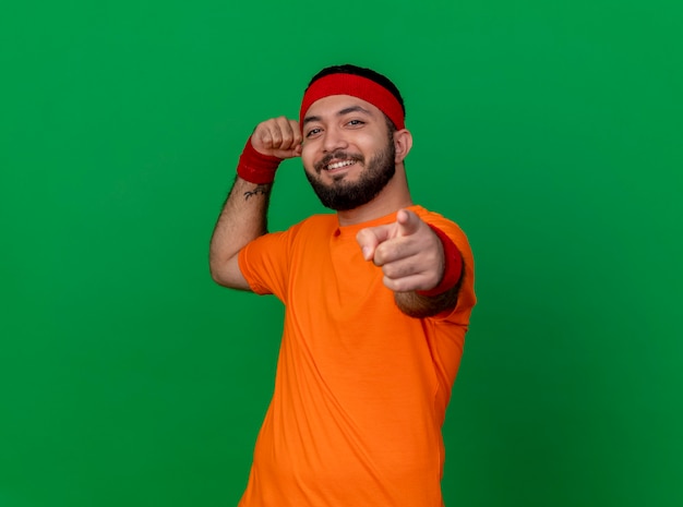 Free photo confident young sporty man wearing headband and wristband showing strong gesture