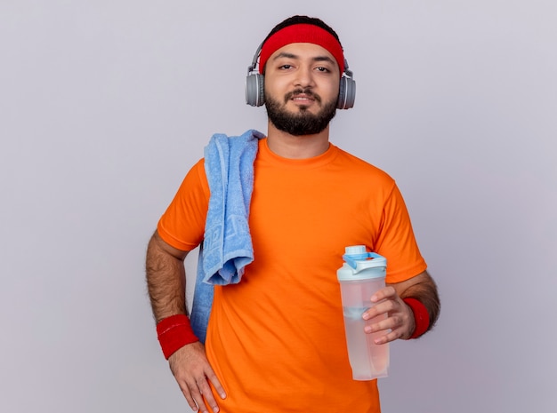 Confident young sporty man wearing headband and wristband with headphones putting hand on hip