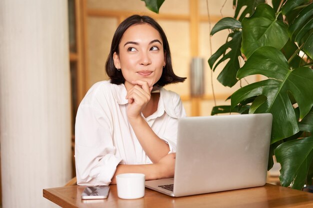 Confident young stylish woman with laptop sitting in cafe and working freelancer in coworking space