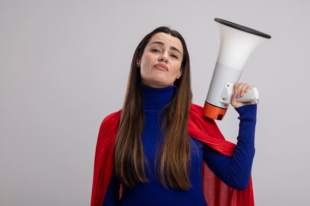 Confident young superhero girl holding loudspeaker isolated on white