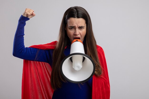 Confident young superhero girl speaks on loudspeaker raising fist isolated on white background