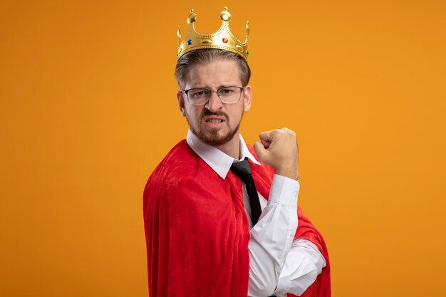 Confident young superhero guy wearing tie and crown with glasses showing yes gesture isolated on orange background