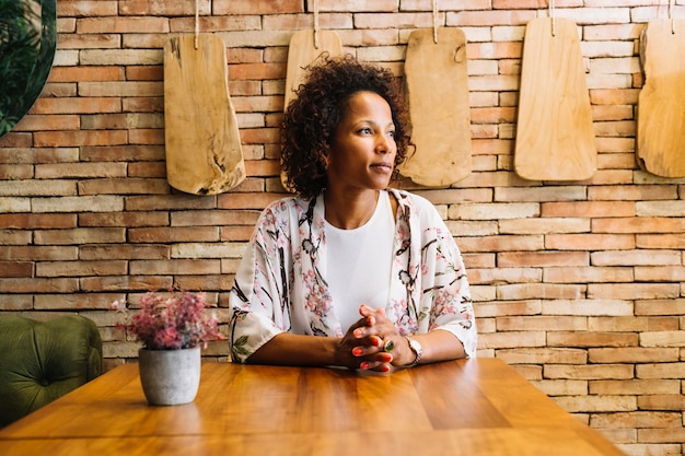 Free photo confident young woman sitting in front of brick wall looking away