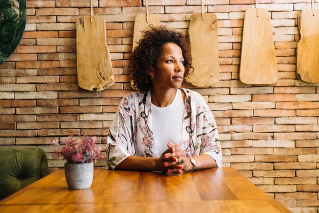 Confident young woman sitting in front of brick wall looking away